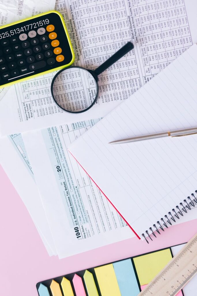 Flat lay of financial documents, calculator, magnifying glass, and notebook on a pastel background.